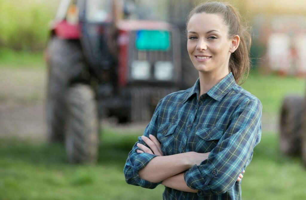 Female farmer smiles into camera standing in front of a farm machine